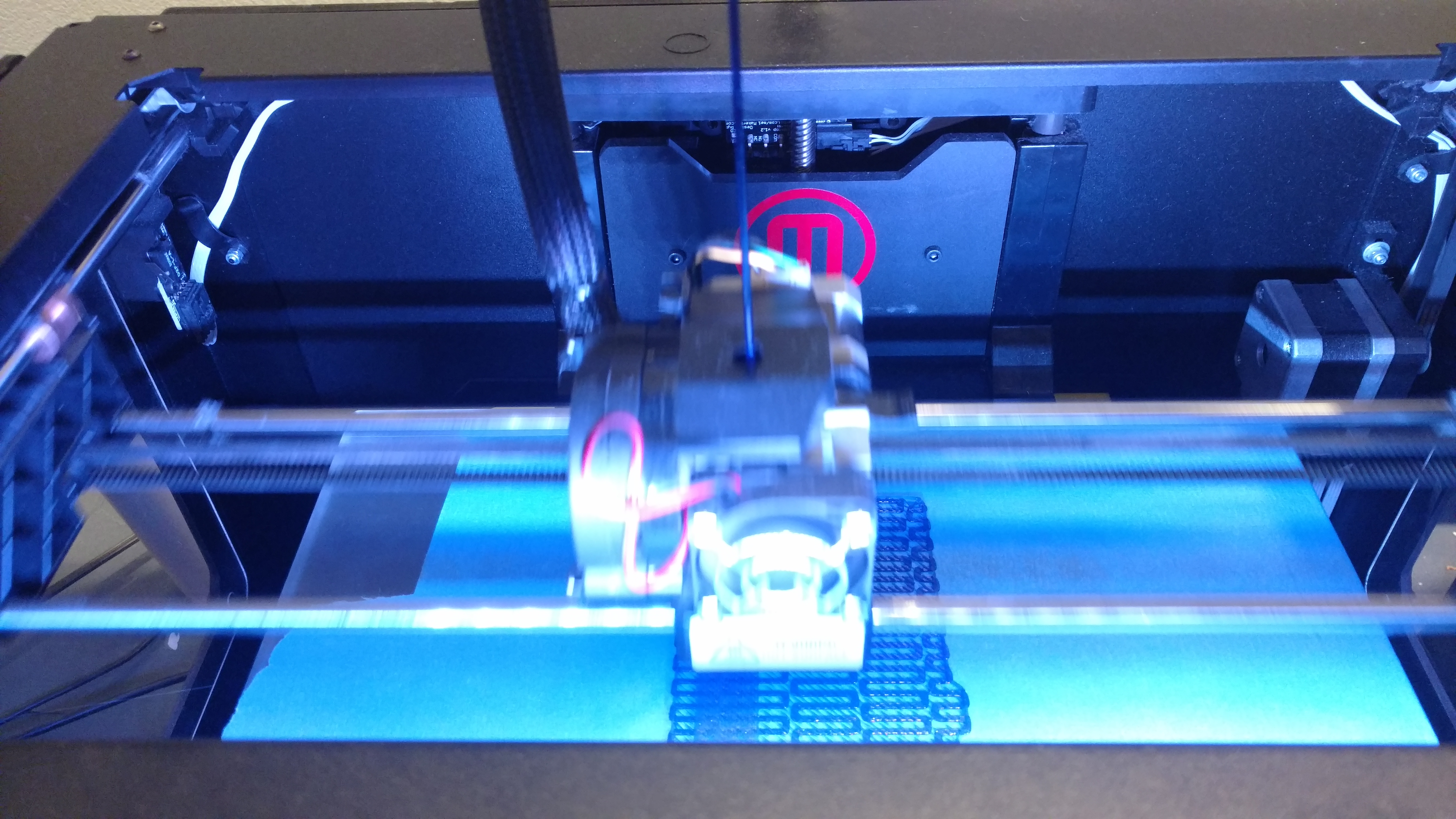 One of the 3D printers in action, lit up in blue
